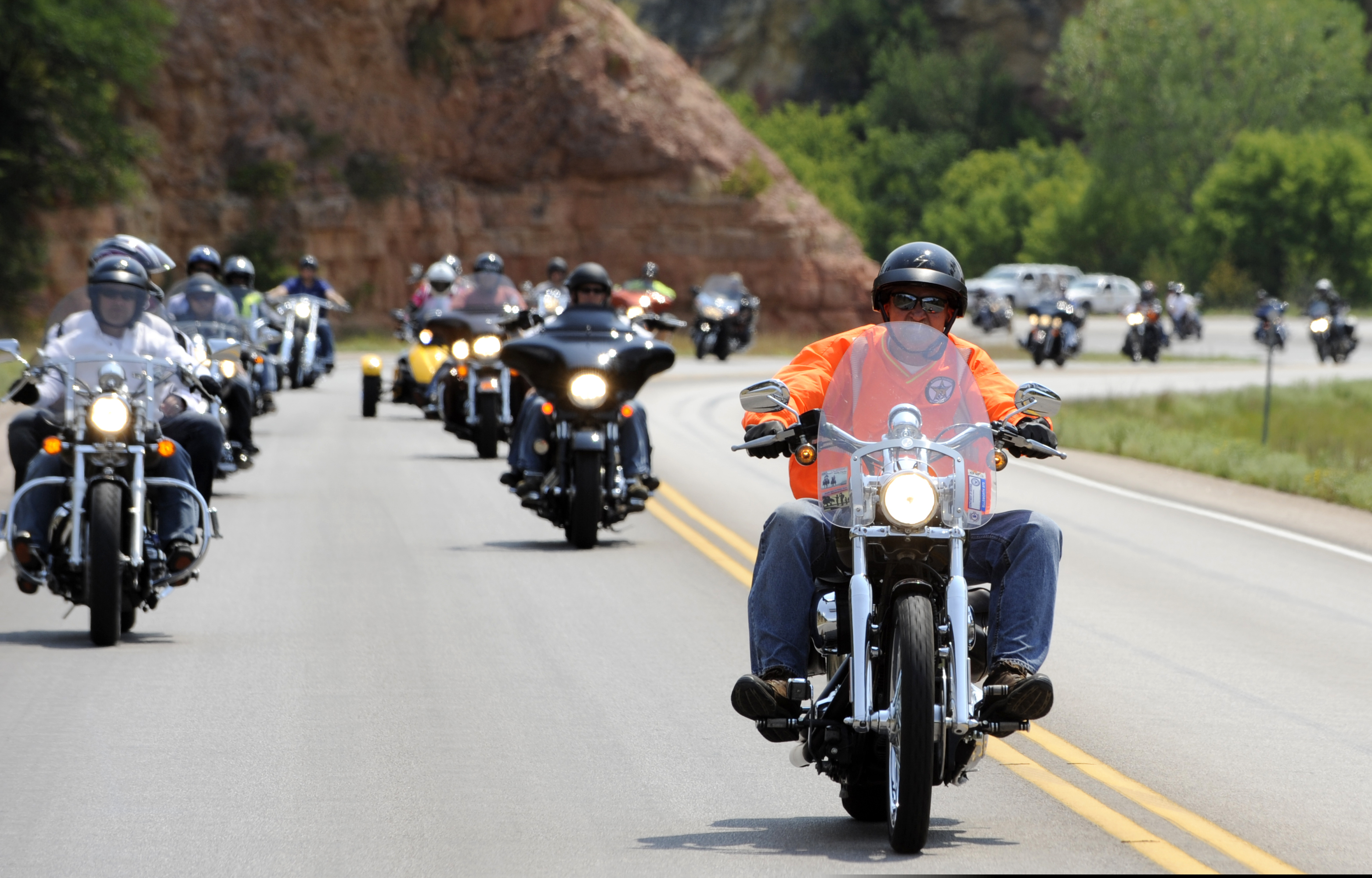 Road Captain Rory Adams at the head of a staggered Harley formation on a Black Hills highway during the 2012 Dakota Thunder Motorcycle Run. High-visibility vest, riders trailing behind in formation.