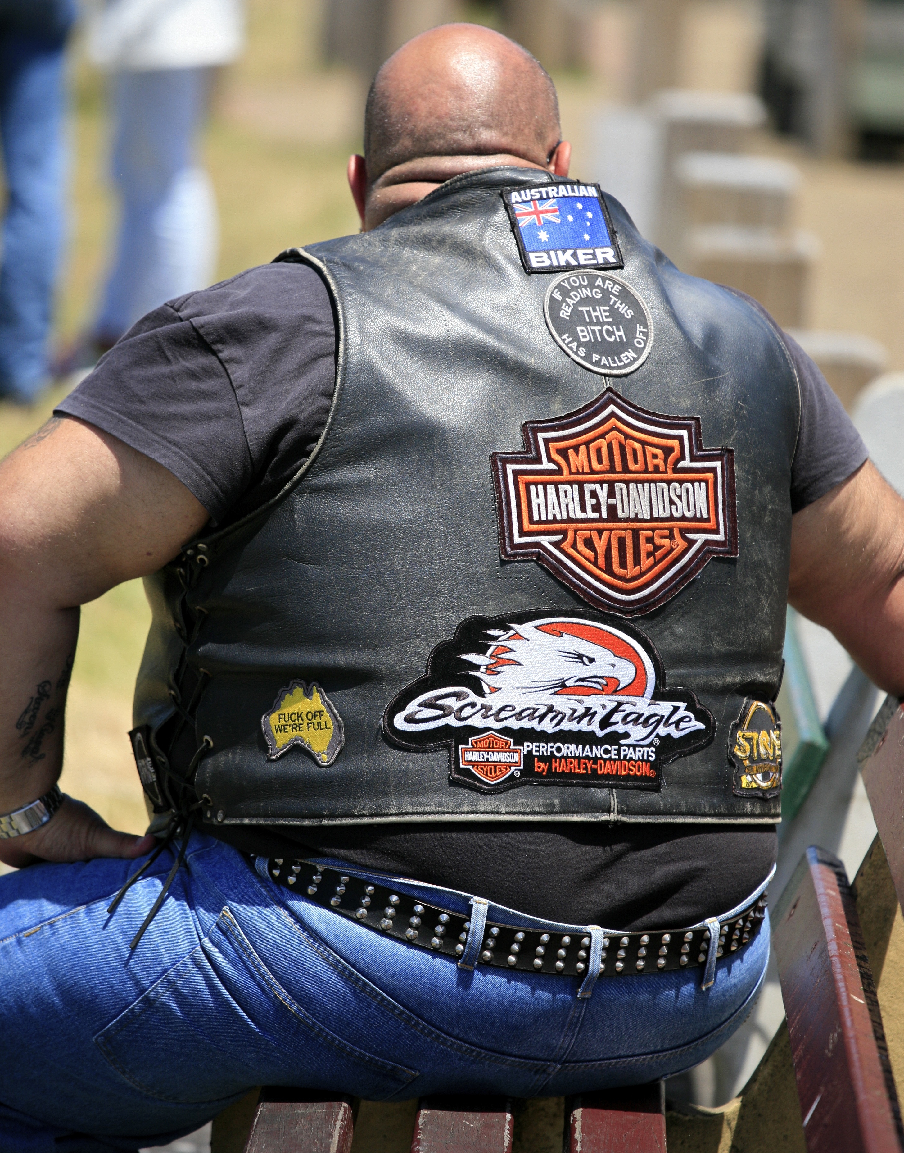 Back of a heavyset Australian rider's leather vest densely covered with Motor Harley-Davidson Cycles patches, Screamin' Eagle patch, and chapter regalia. The visual case for rank earned through mileage.