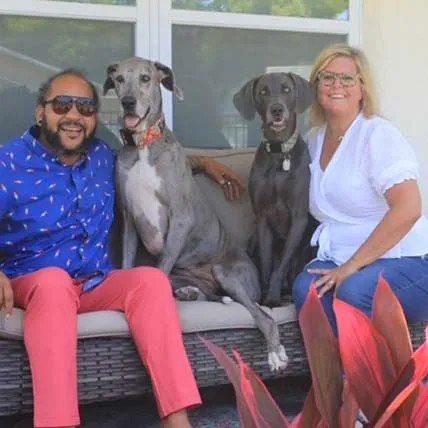 Owners Leigh and Kris Nickens on a patio sofa with their Great Dane Eloise and Weimaraner Walter.
