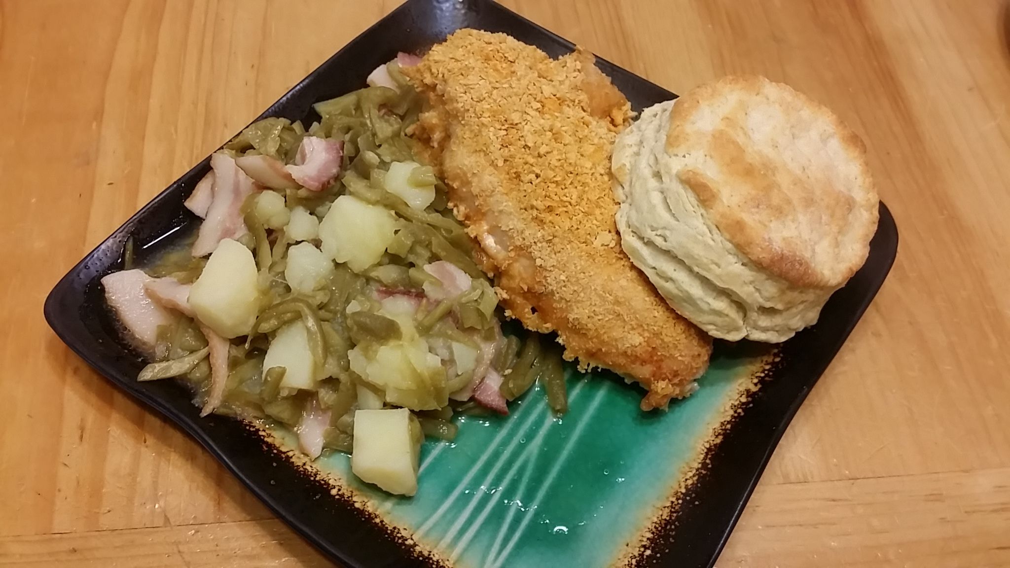Black plate with breaded fried food, sauerkraut with bacon, biscuits, and bright green gelatin dessert on wooden table