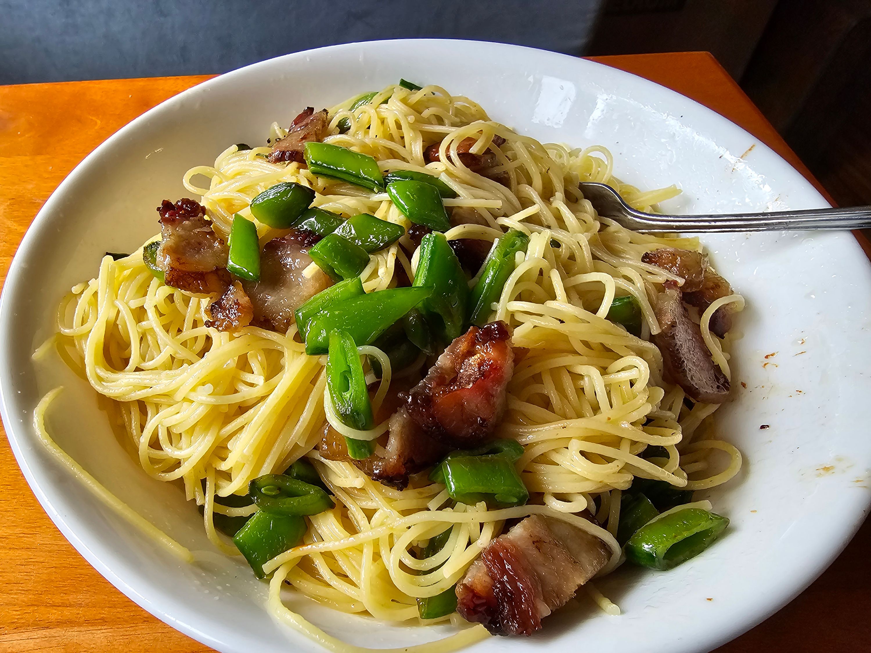 Bowl of spaghetti with bacon, mushrooms, and green onions on a white plate with fork on wooden table