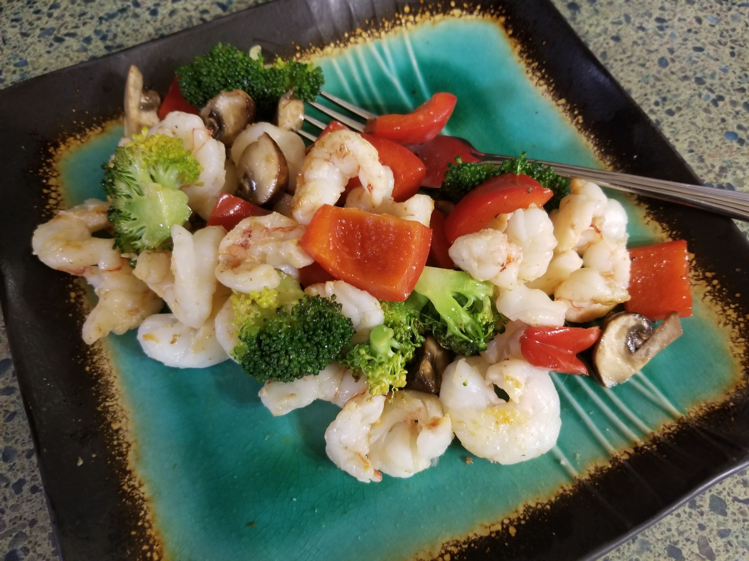 Colorful stir-fried vegetables including shrimp, broccoli, red peppers, and mushrooms served on a turquoise plate with a fork